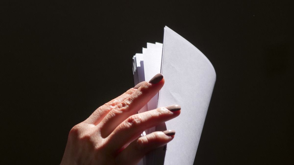 A hand leafs through a stack of blank white pages against a dark background.