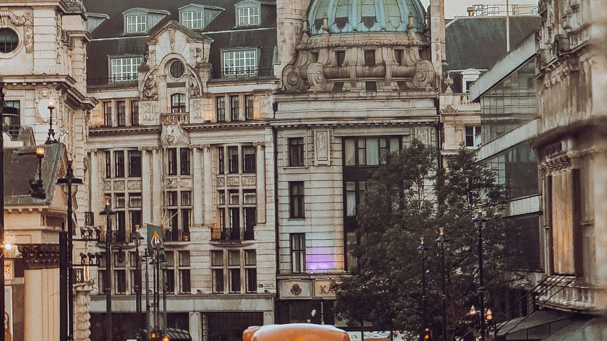 A London street of stone buildings and a copper dome under an overcast sky.