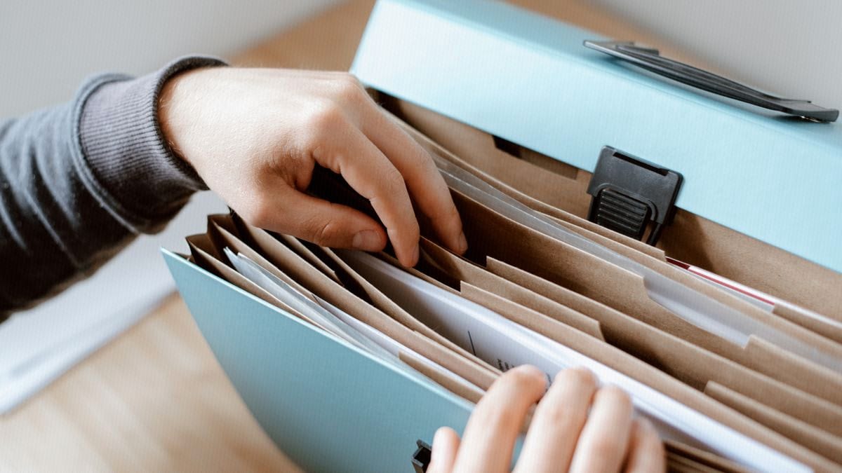 Hands pull a labeled folder from an organized accordion file, reordering which document comes first.